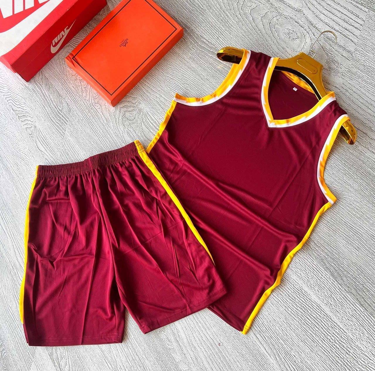 A maroon sleeveless sports jersey and shorts set with gold and white trim, unbranded and ready for team logos